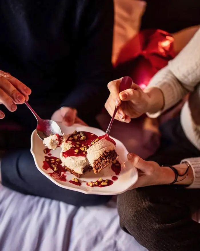Deux personnes partageant un dessert glacé meringue coulis de fruits rouges et éclats de noix, dans une ambiance intimiste