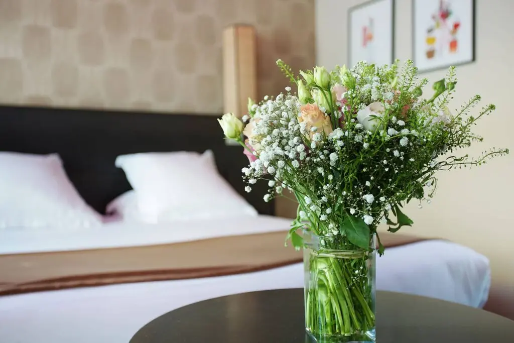 Vase de fleurs fraîches blanches et roses posé sur une table basse, chambre double de l'hôtel Aéro en arrière-plan