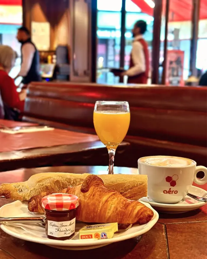 Plateau petit-déjeuner avec croissant, tartines, confiture, jus d'orange et cappuccino, servi en salle au café Aéro