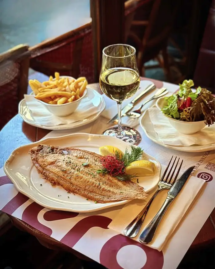 Sole entière grillée servie avec frites et salade verte, accompagnée d'un verre de vin blanc, en salle au restaurant Aéro