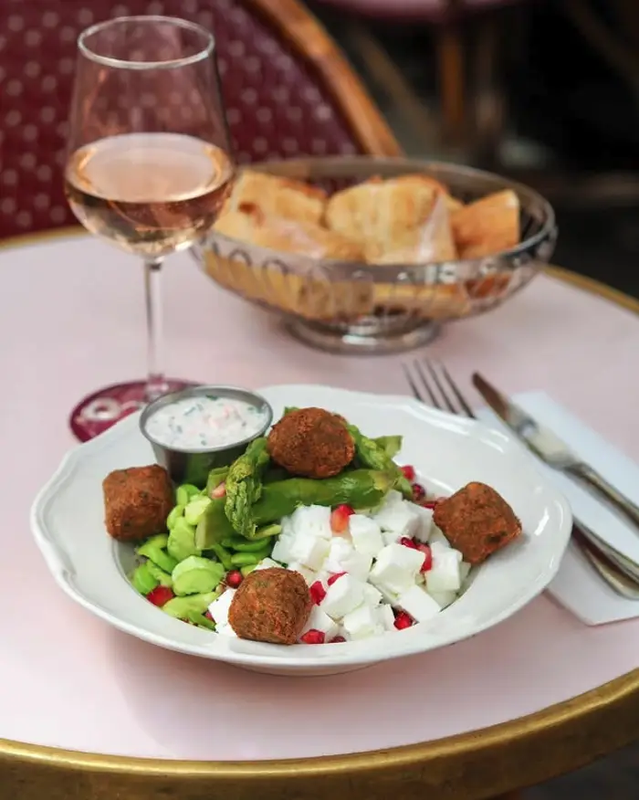 Assiette de salade avec falafels, fêta, asperges et grenades, accompagnée d'un verre de rosé, servie au restaurant Aéro